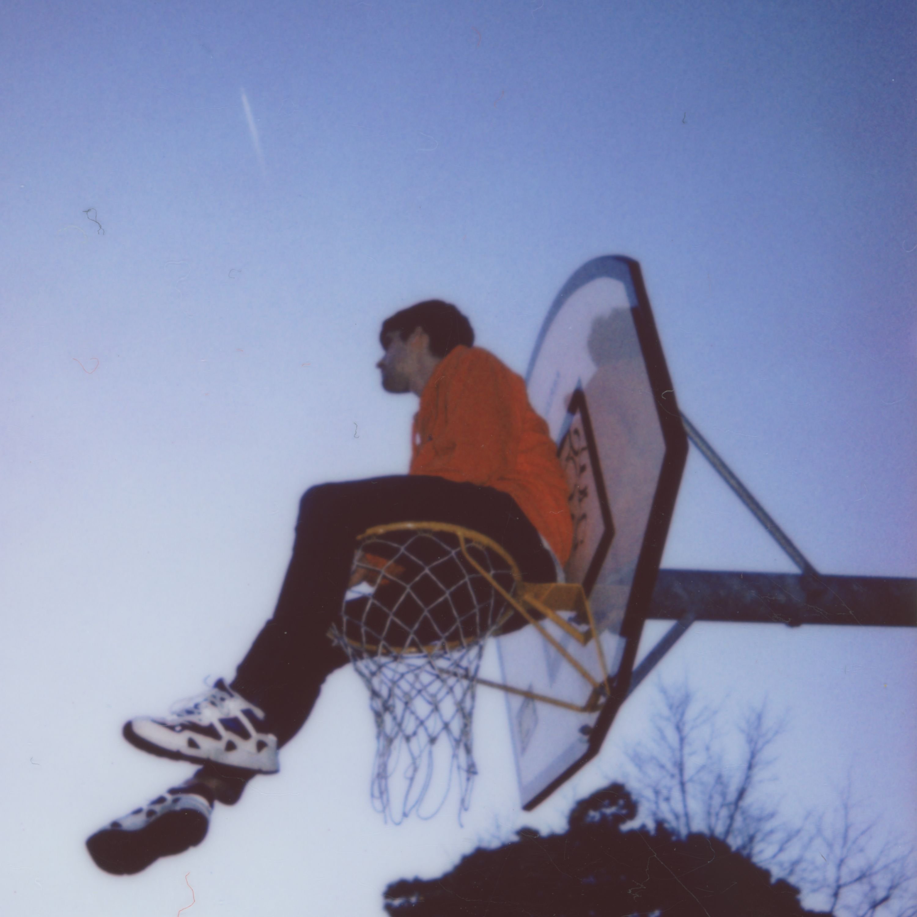 Der Künster Hauskey sitzt auf einem Basketballkorb. Man sieht ihn von unten, der Himmel ist dunkelblau wie kurz nach dem Sonnenuntergang.