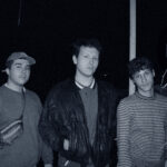 Auf dem Bild sind die drei Bandmember zu sehen: Links Basti, in der Mitte Jonas und rechts daneben steht Colin. ZU dritt stehen sie lässig auf einem Balkon, draußen ist es bereits dunkel.