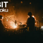 Live-Performance von ORBIT auf einer dunklen Bühne mit Synthesizern und Publikum – Szene aus der ORBIT Mini-Doku