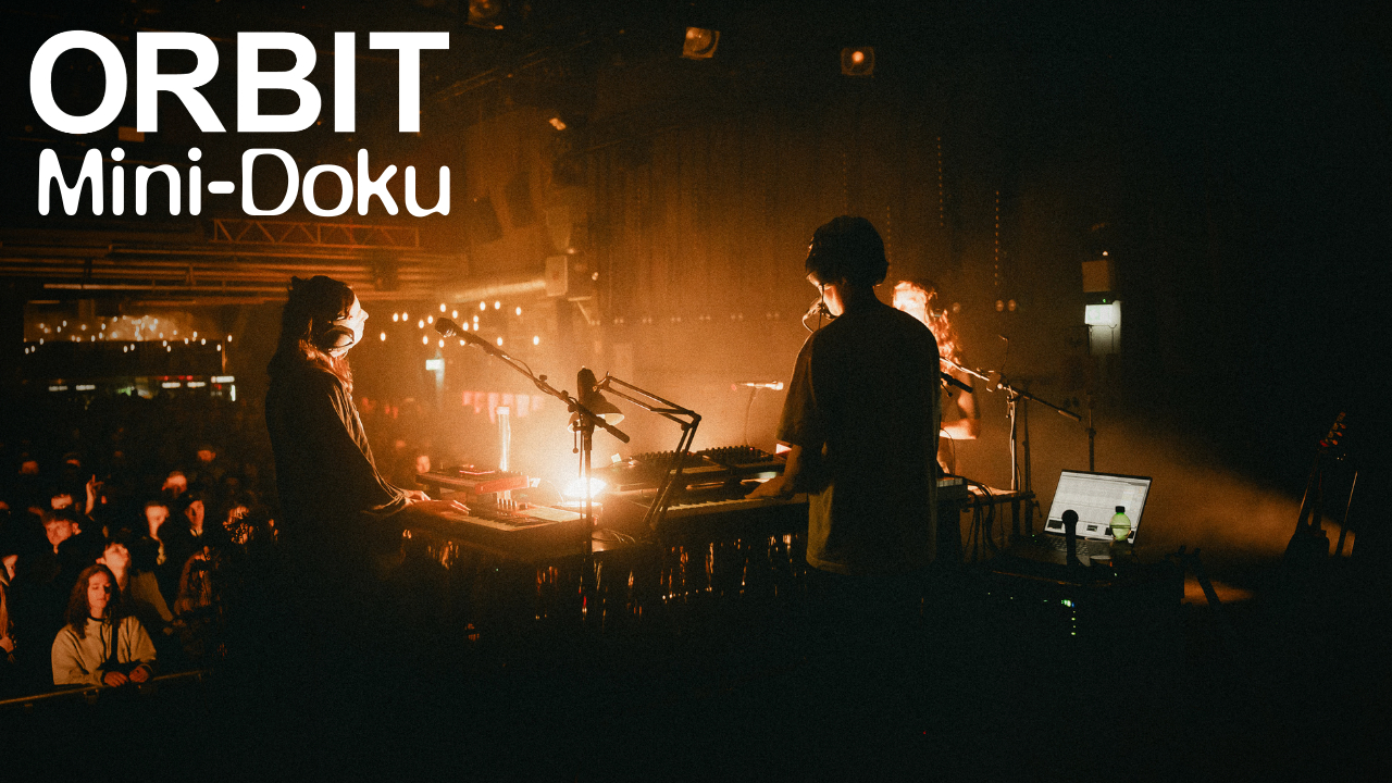 Live-Performance von ORBIT auf einer dunklen Bühne mit Synthesizern und Publikum – Szene aus der ORBIT Mini-Doku